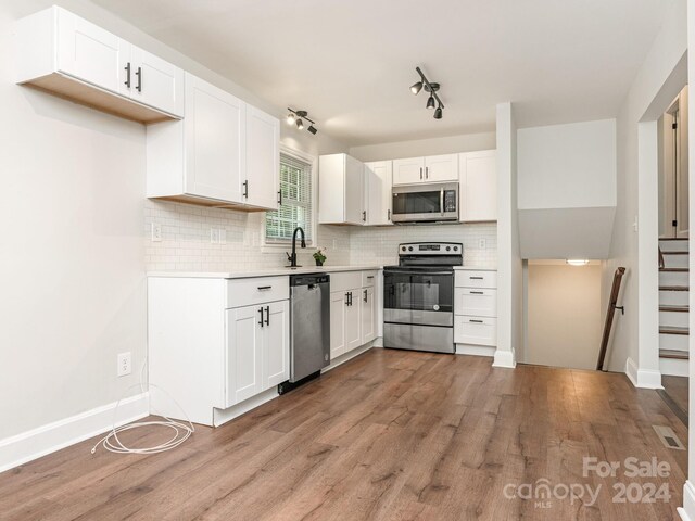 kitchen with light hardwood / wood-style flooring, appliances with stainless steel finishes, white cabinetry, and decorative backsplash