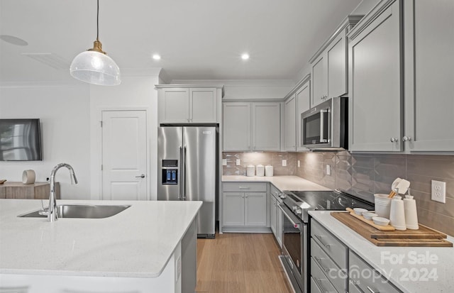 kitchen featuring tasteful backsplash, sink, hanging light fixtures, appliances with stainless steel finishes, and light hardwood / wood-style floors