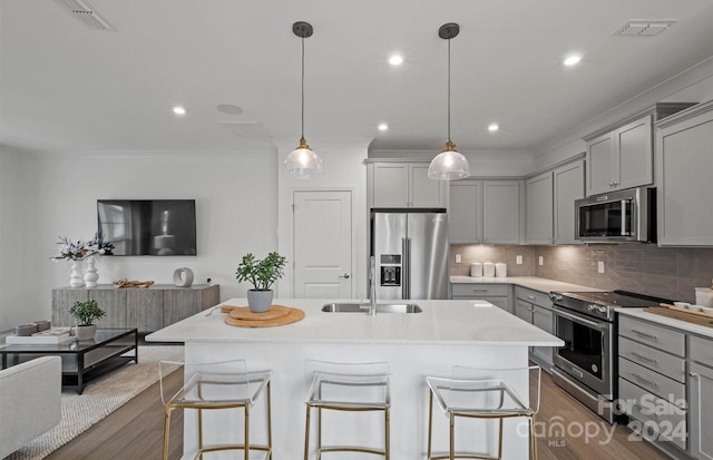 kitchen with gray cabinets, dark hardwood / wood-style flooring, hanging light fixtures, appliances with stainless steel finishes, and a breakfast bar area