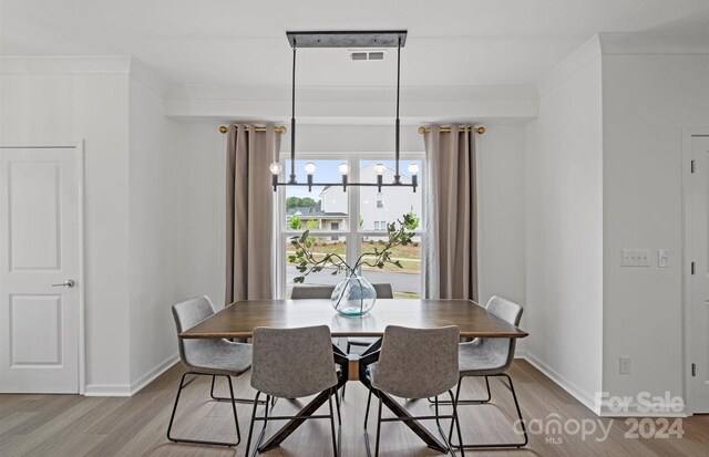 dining space with crown molding, an inviting chandelier, and light wood-type flooring