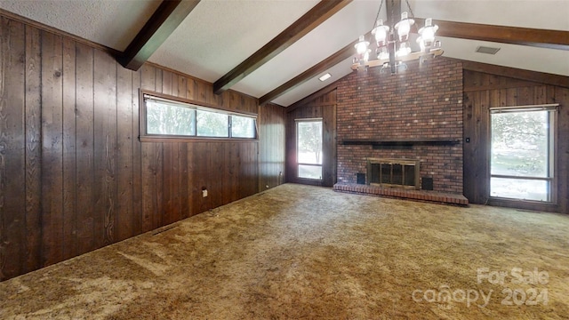 unfurnished living room with wooden walls, a fireplace, lofted ceiling with beams, and a chandelier