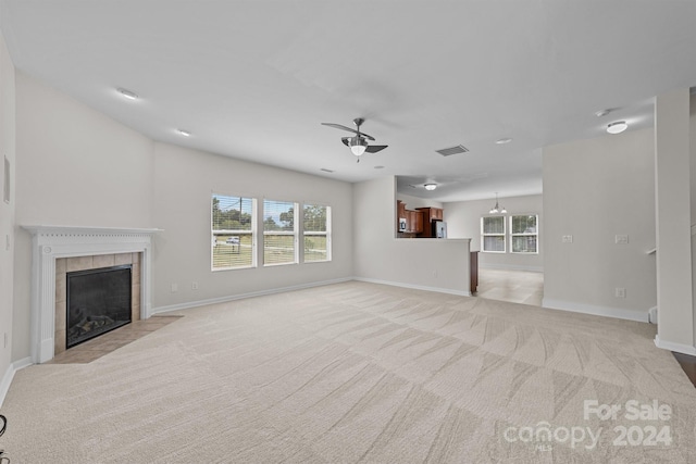 unfurnished living room featuring ceiling fan, a tiled fireplace, and light carpet