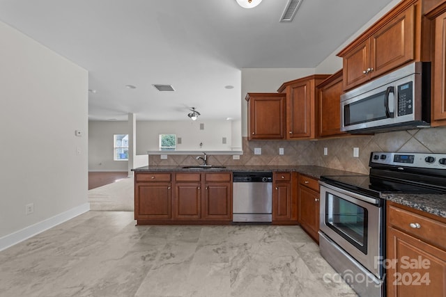 kitchen with backsplash, appliances with stainless steel finishes, kitchen peninsula, sink, and dark stone counters