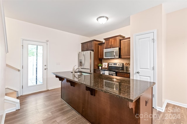 kitchen with dark hardwood / wood-style floors, sink, a kitchen breakfast bar, stainless steel appliances, and dark stone countertops