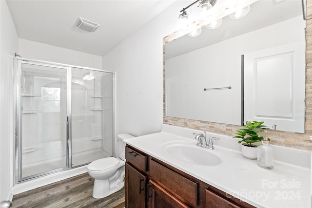 bathroom with wood-type flooring, a shower with shower door, vanity, and toilet