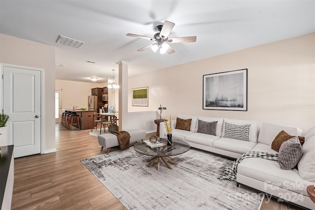 living room with ceiling fan with notable chandelier, decorative columns, and wood-type flooring