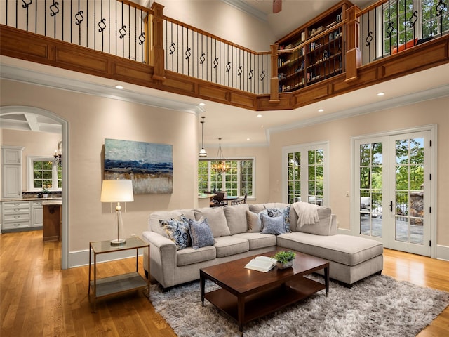 living room featuring an inviting chandelier, french doors, light wood-type flooring, a high ceiling, and ornamental molding