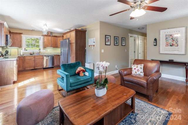 living room with light wood-type flooring, ceiling fan, sink, and a textured ceiling