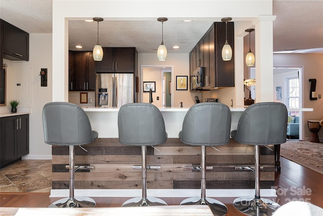 kitchen featuring a textured ceiling, dark brown cabinets, hanging light fixtures, and appliances with stainless steel finishes