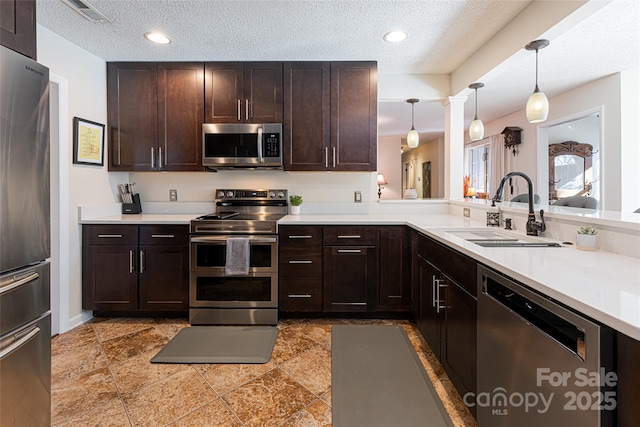 kitchen with a textured ceiling, sink, decorative light fixtures, and appliances with stainless steel finishes