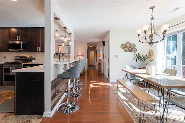 kitchen featuring appliances with stainless steel finishes, dark brown cabinets, decorative light fixtures, a notable chandelier, and dark hardwood / wood-style floors