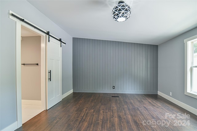 unfurnished room with a barn door and dark wood-type flooring