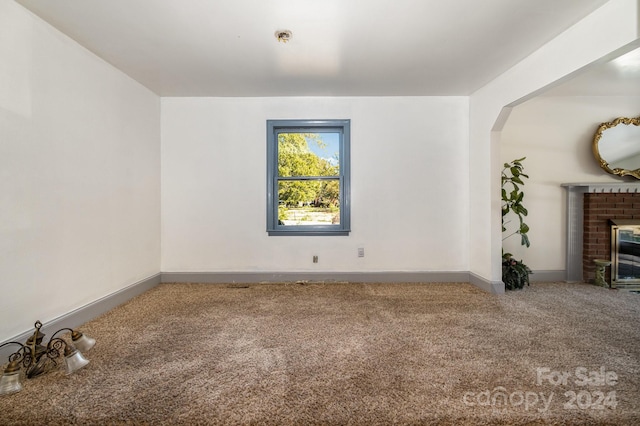 spare room with carpet and a brick fireplace