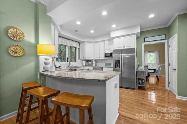 kitchen with stainless steel appliances, white cabinets, light stone counters, and kitchen peninsula