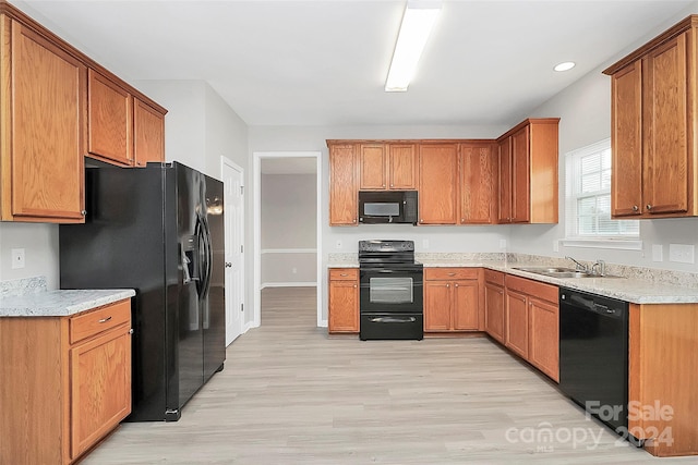 kitchen with light wood-type flooring, black appliances, sink, and light stone countertops