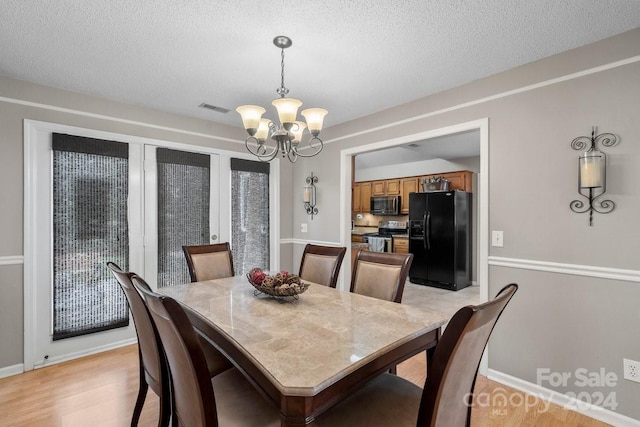 dining area with a textured ceiling, an inviting chandelier, and light hardwood / wood-style floors