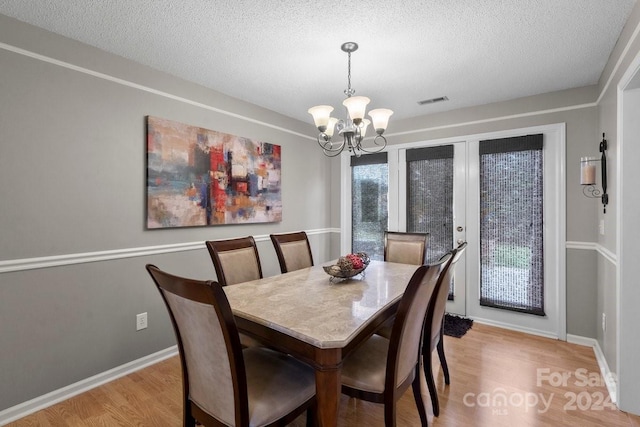 dining space featuring a textured ceiling, light hardwood / wood-style flooring, and an inviting chandelier