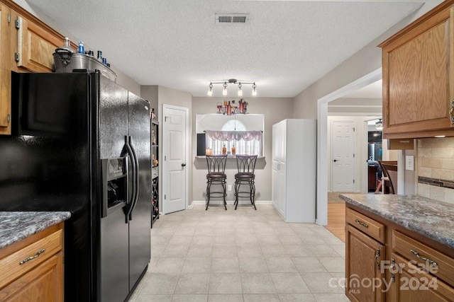 kitchen featuring black fridge, decorative backsplash, dark stone counters, and a textured ceiling