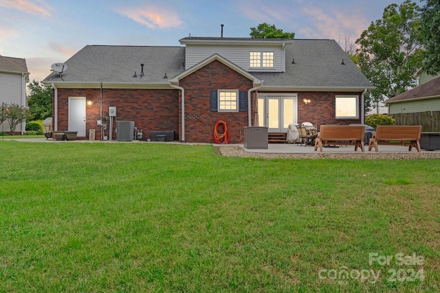 back house at dusk with french doors, a lawn, a patio, and central AC unit