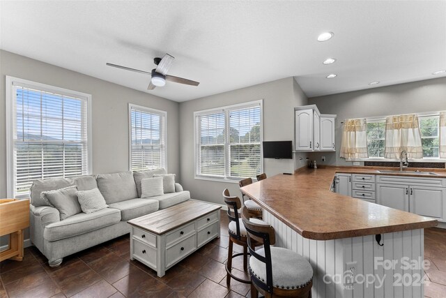 interior space featuring a breakfast bar, kitchen peninsula, sink, ceiling fan, and white cabinets