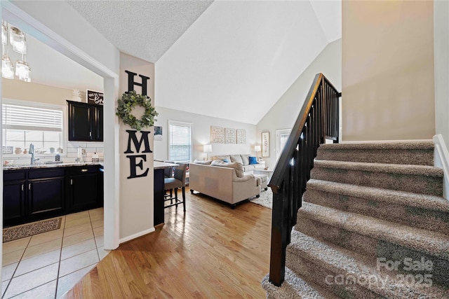 stairway featuring a textured ceiling, wood-type flooring, sink, and vaulted ceiling