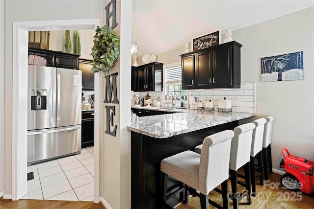 kitchen featuring kitchen peninsula, stainless steel fridge, backsplash, sink, and light tile patterned floors