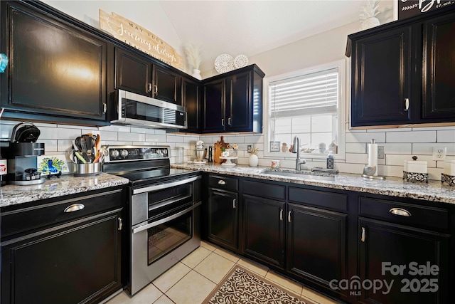 kitchen featuring lofted ceiling, sink, light tile patterned flooring, light stone counters, and stainless steel appliances