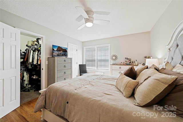 bedroom with a walk in closet, a textured ceiling, ceiling fan, light hardwood / wood-style floors, and a closet