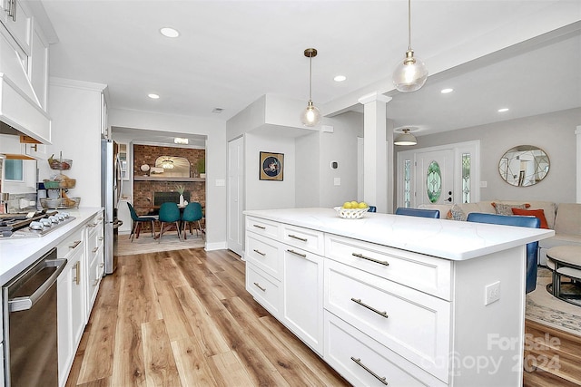 kitchen featuring white cabinetry, light hardwood / wood-style flooring, a center island, hanging light fixtures, and ornate columns