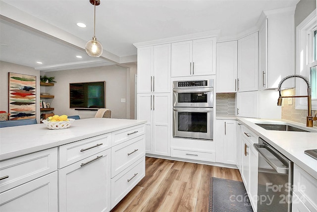 kitchen with decorative light fixtures, sink, appliances with stainless steel finishes, white cabinets, and light hardwood / wood-style floors