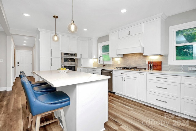 kitchen featuring light wood-type flooring, decorative light fixtures, appliances with stainless steel finishes, custom range hood, and a breakfast bar area