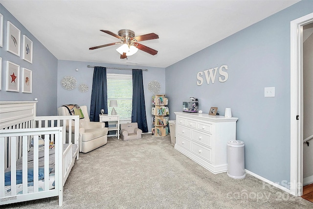 bedroom featuring a nursery area, light carpet, and ceiling fan