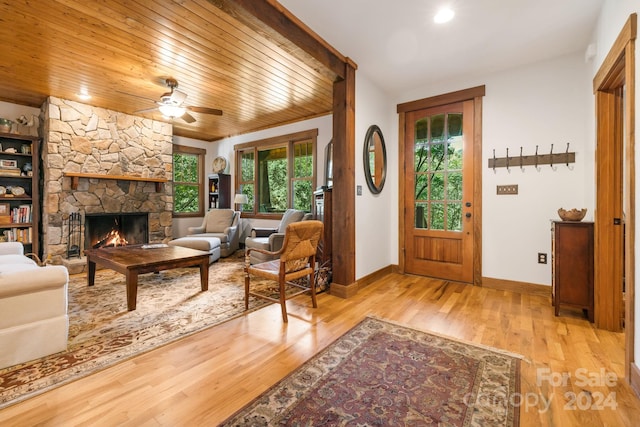 foyer entrance with ceiling fan, a stone fireplace, light wood-type flooring, and wood ceiling