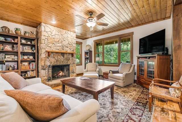 living room with wood ceiling, ceiling fan, ornamental molding, and a stone fireplace