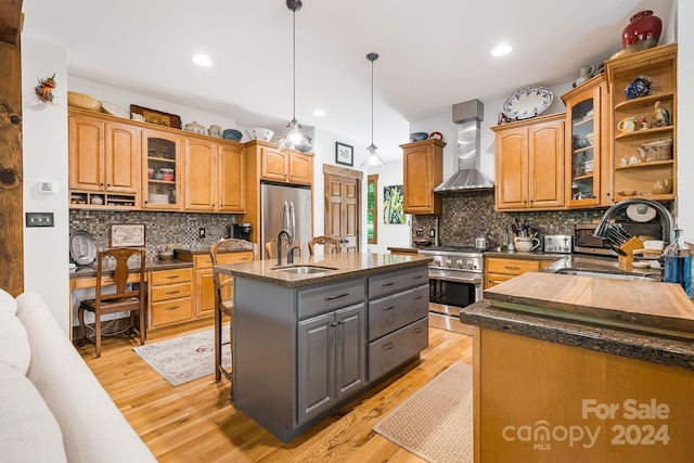 kitchen featuring a kitchen island with sink, sink, hanging light fixtures, wall chimney range hood, and stainless steel appliances