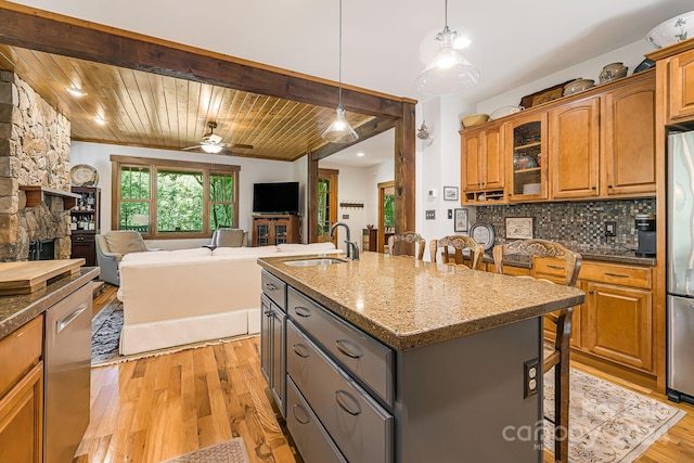 kitchen with wood ceiling, an island with sink, a fireplace, ceiling fan, and light hardwood / wood-style flooring