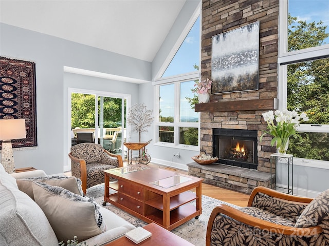 living room featuring a stone fireplace, high vaulted ceiling, and light wood-type flooring