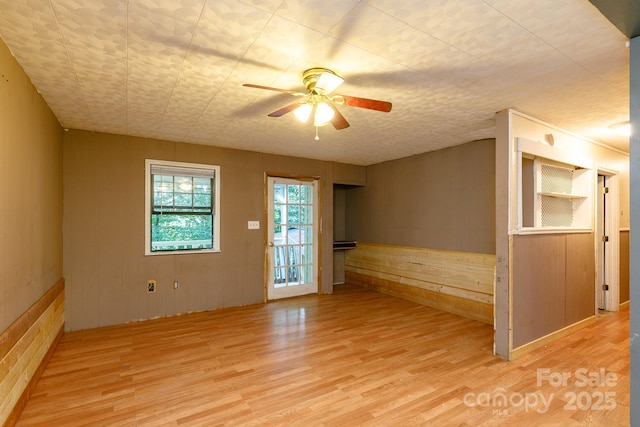 unfurnished room featuring wood walls, ceiling fan, and light wood-type flooring