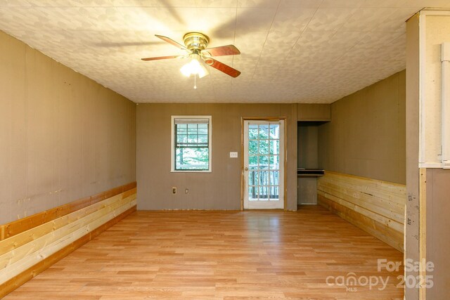 unfurnished room featuring wood walls, ceiling fan, and light wood-type flooring