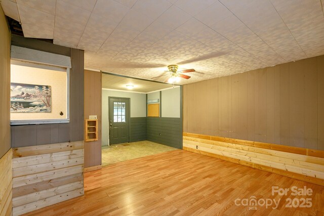 unfurnished room featuring hardwood / wood-style floors, ceiling fan, and wood walls