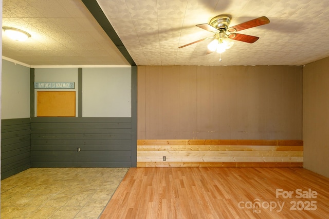 spare room with ceiling fan, wood-type flooring, and wooden walls