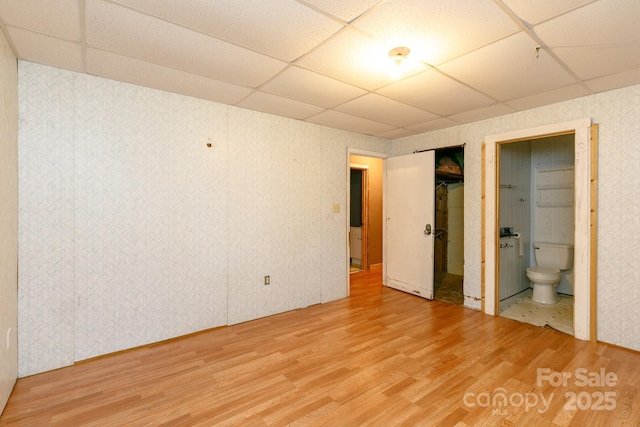 unfurnished bedroom featuring ensuite bathroom, a paneled ceiling, hardwood / wood-style floors, and a closet