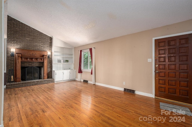 unfurnished living room featuring a textured ceiling, hardwood / wood-style flooring, a fireplace, and built in shelves