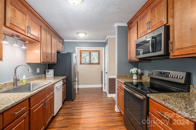 kitchen with dark wood-type flooring, stainless steel appliances, ornamental molding, sink, and light stone countertops