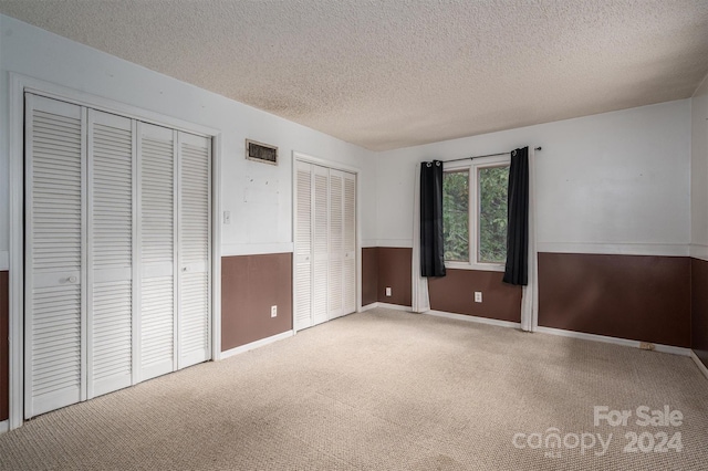 unfurnished bedroom featuring a textured ceiling, multiple closets, and carpet flooring