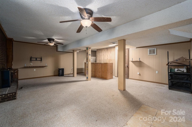 basement featuring a textured ceiling, wooden walls, light colored carpet, and ceiling fan