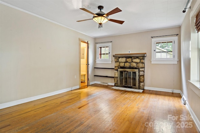 unfurnished living room featuring hardwood / wood-style floors, a stone fireplace, ornamental molding, and a healthy amount of sunlight