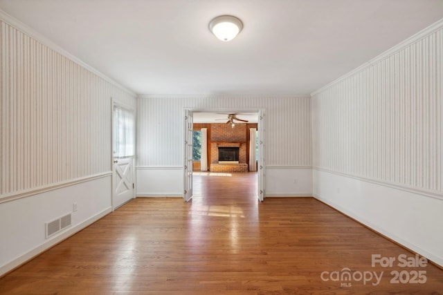 empty room with light hardwood / wood-style flooring, a brick fireplace, ceiling fan, and crown molding