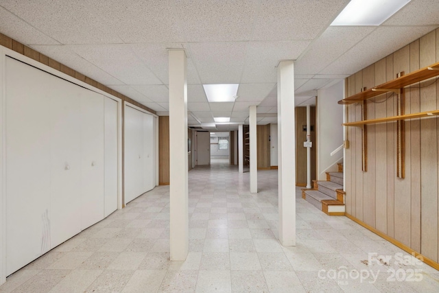 basement featuring a paneled ceiling, wood walls, and elevator