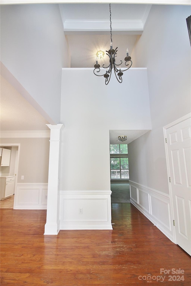 interior space featuring crown molding, wood-type flooring, a high ceiling, and a notable chandelier